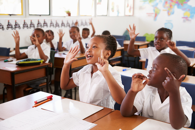 Enthusiastic primary school pupils raising hands in class
